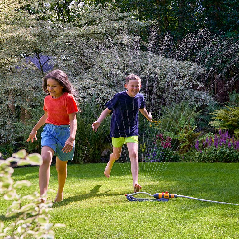 Hozelock Rectangular Sprinkler on lawn with children running through the spray